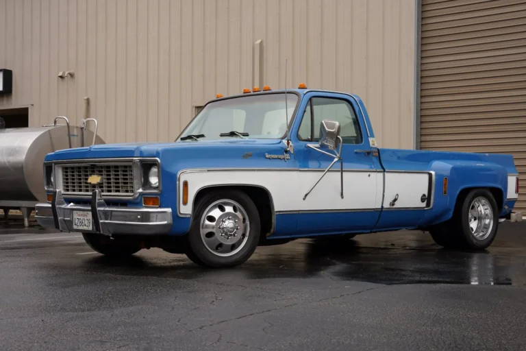 Blue and white square-body Chevy Cheyenne C10 dually on polished wheels, parked in front of a warehouse
